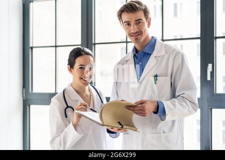 Portrait de deux médecins dévoués souriant et regardant la caméra tout en tenant une tablette et un dossier avec des dossiers médicaux Banque D'Images