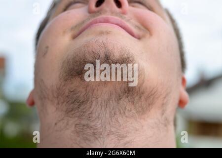 Jeune homme non rasé avec une barbe plus sage en gros plan sur sa gorge et des poils du visage à l'extérieur contre le ciel gris Banque D'Images