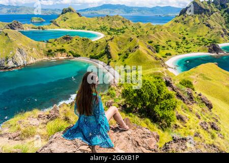 Vue arrière d'une jeune femme admirant la magnifique vue sur l'île de Padar, assis sur le sommet d'une montagne volcanique, pendant les vacances d'été en Indonésie Banque D'Images