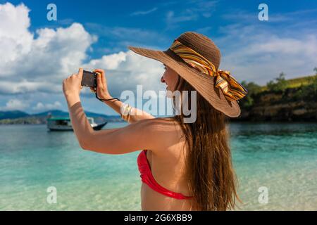 Jeune femme gaie prenant des photos avec un appareil photo compact par une journée ensoleillée pendant les vacances d'été à Komodo Island, Indonésie Banque D'Images