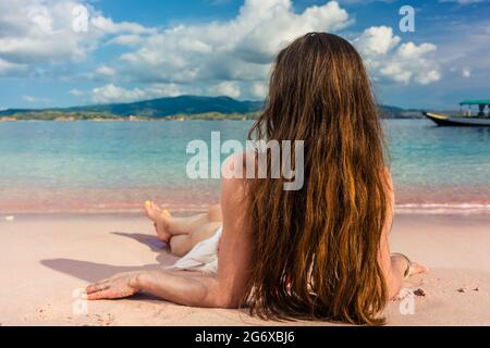 Vue arrière d'une jeune femme avec de longs cheveux bruns rêvant de jour tout en s'étendant sur la plage dans un jour chaud de l'été pendant les vacances à l'île de Komodo, dans Banque D'Images