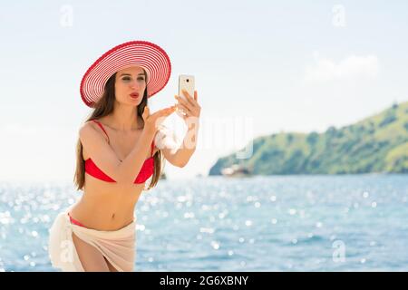 Belle jeune femme soufflant un baiser tandis que le partage sur les médias sociaux une photo ou un live selfies vidéo pendant les vacances d'été dans l'île de Flores, en Indonésie Banque D'Images