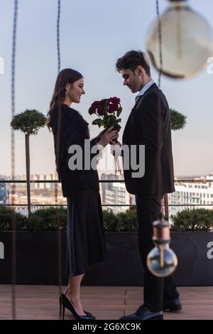 homme sur toute la longueur donnant des roses rouges à une femme heureuse en veste en fausse fourrure Banque D'Images