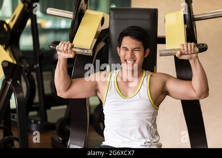 Portrait d'un jeune homme fort et beau sourire tout en s'exerçant pour des bras muscles pendant de supérieur-corps routine à un club de remise en forme avec équipement moderne Banque D'Images