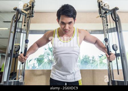 Faible angle de vue portrait d'un bel homme asiatique à la concentration avec le bas tout en exerçant un cable crossover de muscles de coffre dans la salle de sport Banque D'Images