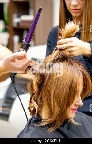Deux coiffures utilisant le fer à friser sur les clients cheveux longs bruns dans un salon de beauté Banque D'Images