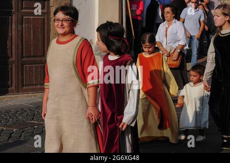 Les enfants locaux en costume médiéval coloré, conduits par un adulte, tiennent la main pendant qu'ils attendent sur la Piazza Guglielmo Marconi à Anagni, Lazio, Italie, pour un signal de descendre dans un pageant historique d'août en l'honneur de Saint Magnus d'Anagni, leur Saint patron. Le spectacle rappelle également le passé d'Anagni en tant que ville des Papes, la résidence d'été des empereurs romains et du pontife cherchant un refuge plus frais face à la chaleur estivale de Rome. Banque D'Images