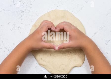 Cœur des mains des enfants sur le fond du test. Un enfant pétrit de la pâte à biscuits dans la cuisine. Pâte de sélénium pour la modélisation, pour enfants Banque D'Images