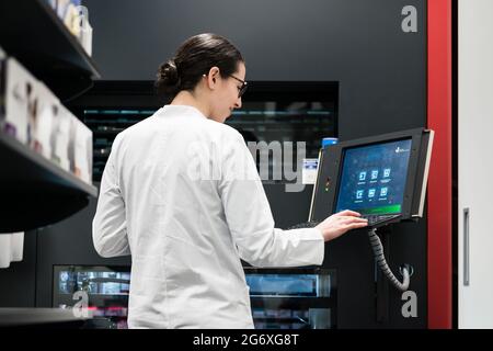 Low-angle rear view of an experienced female pharmacist using a computer while managing the drug stock in a contemporary pharmacy with modern technolo Stock Photo