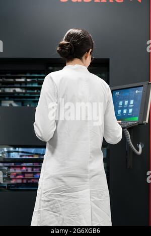 Low-angle rear view of an experienced female pharmacist using a computer while managing the drug stock in a contemporary pharmacy with modern technolo Stock Photo