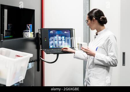 Low-angle rear view of an experienced female pharmacist using a computer while managing the drug stock in a contemporary pharmacy with modern technolo Stock Photo