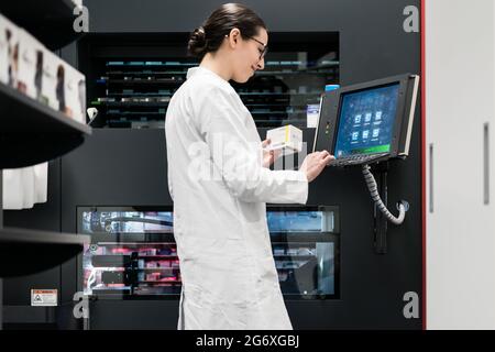 Low-angle rear view of an experienced female pharmacist using a computer while managing the drug stock in a contemporary pharmacy with modern technolo Stock Photo