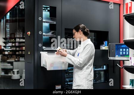 Low-angle rear view of an experienced female pharmacist using a computer while managing the drug stock in a contemporary pharmacy with modern technolo Stock Photo