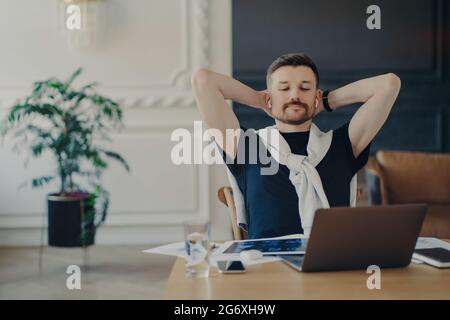 Un jeune homme d'affaires qui regarde des vidéos sur un ordinateur portable se sent détendu lorsqu'il travaille de chez lui Banque D'Images