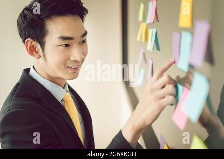 Smiling young businessman pointing at sticky notes sur le babillard Banque D'Images