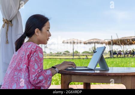 Femme indépendante assise dans un café en plein air et travaillant sur un ordinateur portable. Banque D'Images