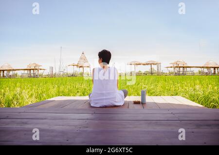 Femme assise sur un sol en bois avec thermos bouteille regarder un magnifique paysage. Banque D'Images