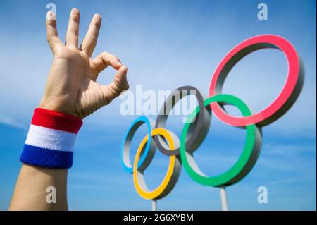 RIO DE JANEIRO - MARS, 2016: Un athlète portant un bracelet rouge, blanc et bleu fait un geste correct devant les anneaux olympiques. Banque D'Images