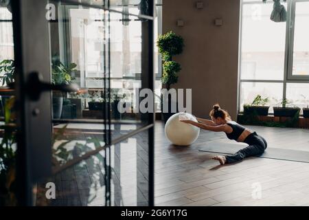Jeune femme s'exerçant avec le fitball, faisant des exercices d'étirement dans le studio de fitness Banque D'Images