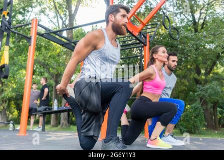 Vue latérale sur toute la longueur de trois amis déterminés faisant des exercices d'étirement pour les jambes, comme échauffement ou de rafraîchir la routine à l'extérieur dans un fitness moderne Banque D'Images