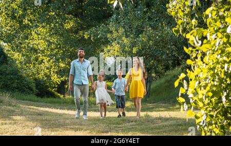 Sur toute la longueur d'une famille heureuse avec deux enfants portant des vêtements d'été décontracté tout en tenant les mains au cours de promenade dans le parc de loisirs Banque D'Images