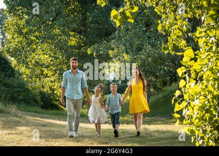 Sur toute la longueur d'une famille heureuse avec deux enfants portant des vêtements d'été décontracté tout en tenant les mains au cours de promenade dans le parc de loisirs Banque D'Images