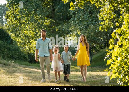 Sur toute la longueur d'une famille heureuse avec deux enfants portant des vêtements d'été décontracté tout en tenant les mains au cours de promenade dans le parc de loisirs Banque D'Images