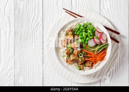 bol à poke de tofu vegan avec riz basmati, haricots édamames, radis, concombre finement tranché et carottes dans un bol blanc avec baguettes, vue horizontale Banque D'Images