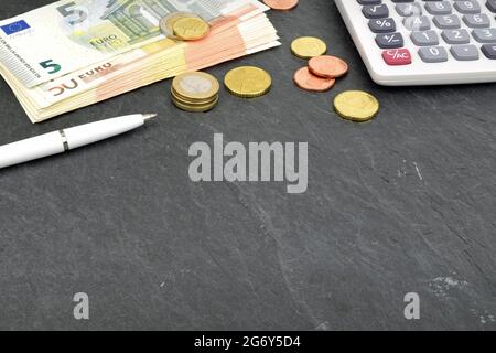 Un arrangement de billets d'euros, pièces et calculatrice sur ardoise. Banque D'Images