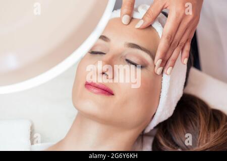 D'un grand angle de vue le visage d'une femme détendue smiling sous l'avantages de massage facial anti-âge dans un centre de beauté contemporaine Banque D'Images