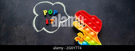 Bannière avec pop il dinosaure jouet couleurs arc-en-ciel sur un fond noir avec des lettres multicolores et l'inscription - Pop il dans une bulle de parole. Banque D'Images