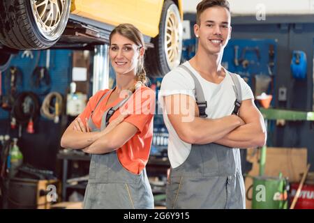 Portrait de deux mécaniciens qualifiés looking at camera avec confiance tout en portant l'ensemble gris dans un atelier de réparation automobile moderne avec de l'expérience Banque D'Images