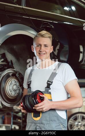 Faible angle de vue portrait d'un certain jeune auto mechanic holding un nouveau système de suspension pneumatique, tout en travaillant dans le tuning d'une voiture dans un moderne autom Banque D'Images