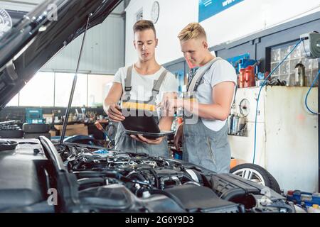 Mécanicien automobile expérimenté utilisant un ordinateur portable pour lire et interpréter les codes d'erreur de moteur à côté d'un apprenti dans un atelier de réparation automobile moderne Banque D'Images