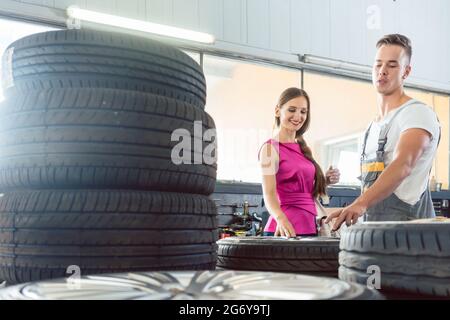 Belle auto mechanic aide une clientèle féminine de choisir entre différents pneus de haute qualité dans un atelier de réparation automobile contemporaine Banque D'Images