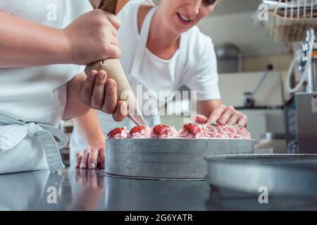 Pâtissier ou pâtissiers gâteaux de finition avec poche à douille, close-up sur les mains Banque D'Images