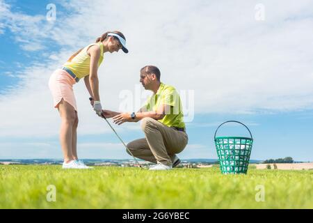 Longueur pleine vue latérale d'une jeune femme tenant un club de fer, tout en exerçant l'oscillation de golf a aidé par son instructeur expérimenté à l'extérieur sur vert gr Banque D'Images