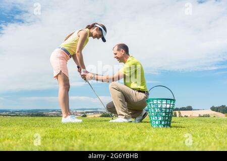 Longueur pleine vue latérale d'une jeune femme tenant un club de fer, tout en exerçant l'oscillation de golf a aidé par son instructeur expérimenté à l'extérieur sur vert gr Banque D'Images