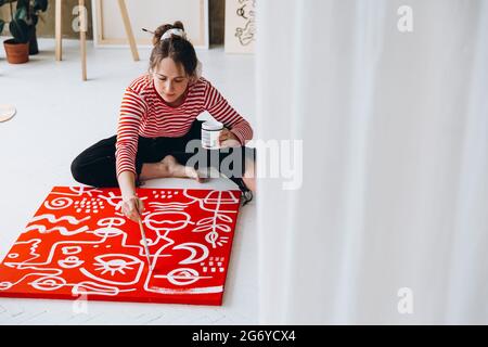 Une jeune femme peint sur toile en étant assise sur le sol Banque D'Images