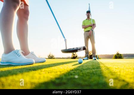 Balle de golf en focus sélectif sous le club de putter d'une femme jouant sur le vert de mise en classe avec un enseignant expérimenté Banque D'Images