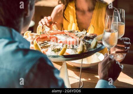 Gros plan d'huîtres fraîches et de crabes servis sur glace avec citron à la table d'un couple romantique amoureux, célébrant avec du champagne dans un restaurant branché Banque D'Images