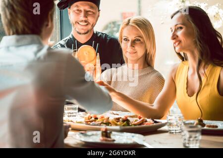 Un chef expérimenté souriant a été félicité pour la délicieuse cuisine de quatre jeunes à la table d'un restaurant chic et branché Banque D'Images