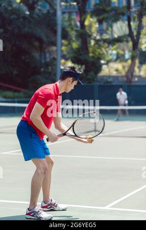 Vue latérale d'un joueur de tennis asiatique prêt à servir au début d'un match mixte en double sur un court de tennis professionnel Banque D'Images