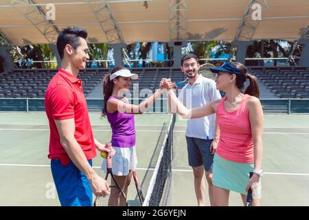 Quatre jeunes joueurs de tennis et de compétition mettant les mains ensemble au-dessus du net comme un geste de fair-play avant un match mixte en double Banque D'Images