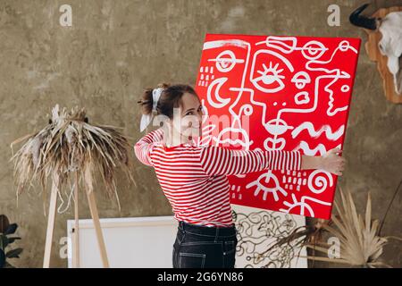 Femme souriante tenant une toile rouge avec un dessin abstrait Banque D'Images