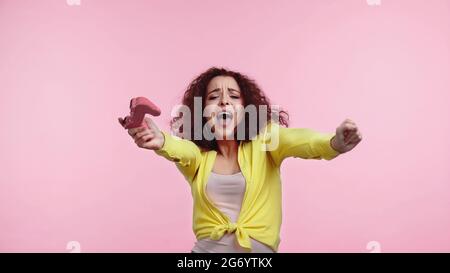 KIEV, UKRAINE - 30 JUIN 2021 : jeune femme excitée tenant le joystick et se réjouissant isolée sur rose Banque D'Images