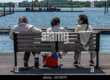 trois personnes âgées indiennes ou asiatiques assis sur un banc de bois discutant et parlant ensemble lors d'une journée ensoleillée en regardant l'eau au bord de la mer Banque D'Images