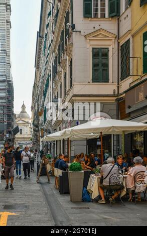 Via San Lorenzo, l'une des rues principales, avec des gens qui déjeunent dans un restaurant en plein air et l'église de Jésus en arrière-plan, Gênes, Italie Banque D'Images