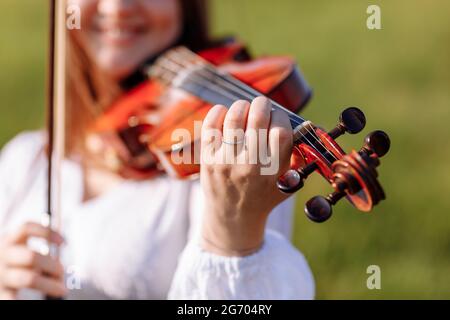 la petite fille joue du violon à l'extérieur avec le jardin en arrière-plan le jour ensoleillé de l'été. Image avec mise au point sélective et espace de copie Banque D'Images