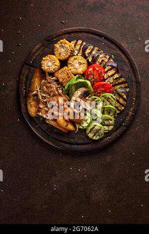 une grande portion de légumes et de champignons frits de couleur sur un plateau en bois sur fond sombre. Banque D'Images